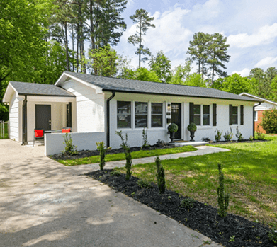 A white house with a driveway and trees in the background.